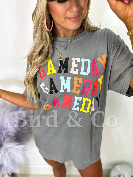 Gray t-shirt with 'GAMEDAY' in colorful letters worn by a person.