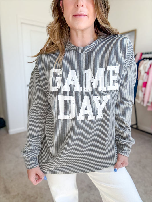 Women’s gray and white striped “GAME DAY” long-sleeve graphic sweatshirt paired with white pants – sporty casual game day outfit.