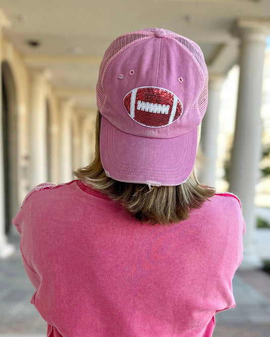 A person wearing a pink sequin football hat with a prominent red and white football design on the front, turned around with their back towards the camera.