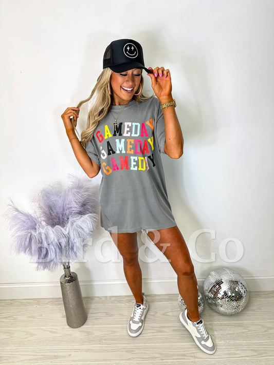 Woman wearing a gray t-shirt dress with colorful text and a black cap, standing in a room with decorative items.